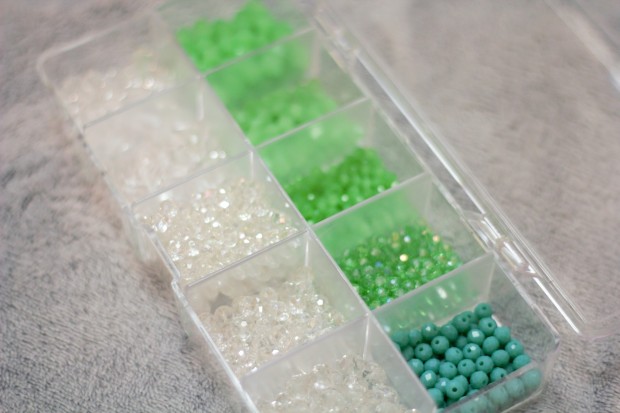 Different shades of light green crystals and clear crystals sparkly in a container on a light grey background